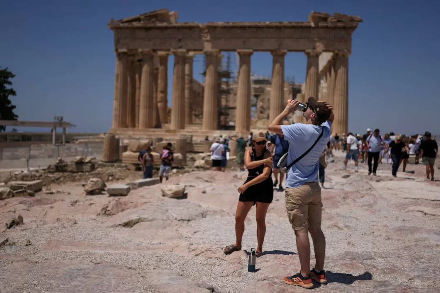 سائح يشرب الماء خلال زيارته لمعبد البارثينون في ظل موجة حرّ تضرب أثينا في اليونان يوم 27 يونيو 2025 (رويترز)