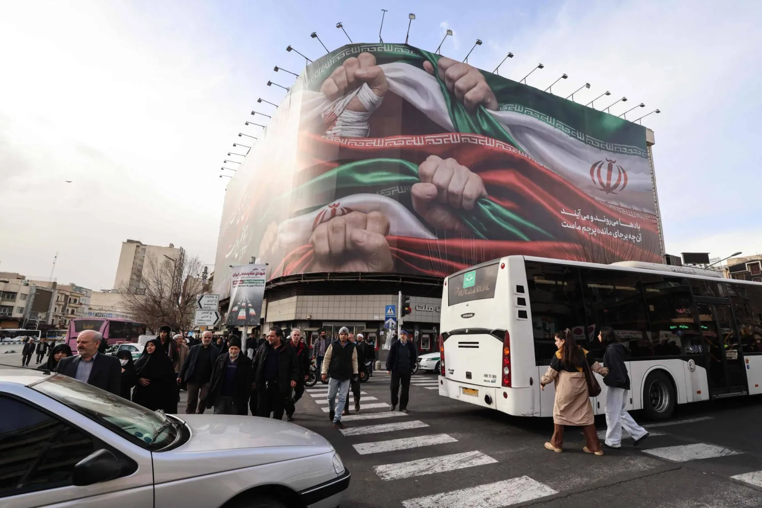 People walk past a large patriotic banner depicting the Iranian flag on Enghelab Square in Tehran on January 14, 2026.  (Photo by ATTA KENARE / AFP)