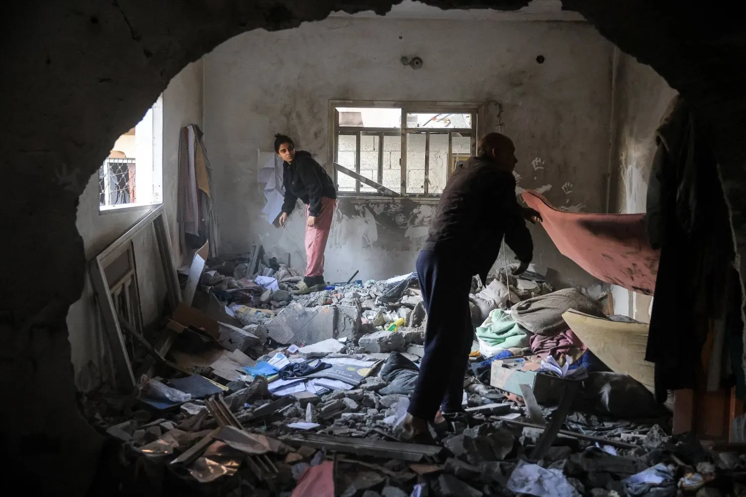 فلسطينيون ينتشلون أغراضاً من منزل بعد هجوم عسكري إسرائيلي غرب دير البلح وسط قطاع غزة (أ.ف.ب)