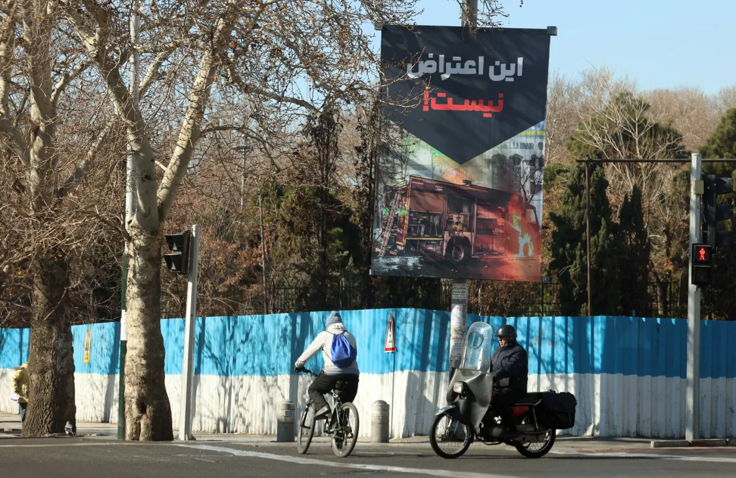 إيرانيون يسيرون بجانب لافتة مكتوب عليها باللغة الفارسية «هذا ليس احتجاجاً» في أحد شوارع طهران (إ.ب.أ)