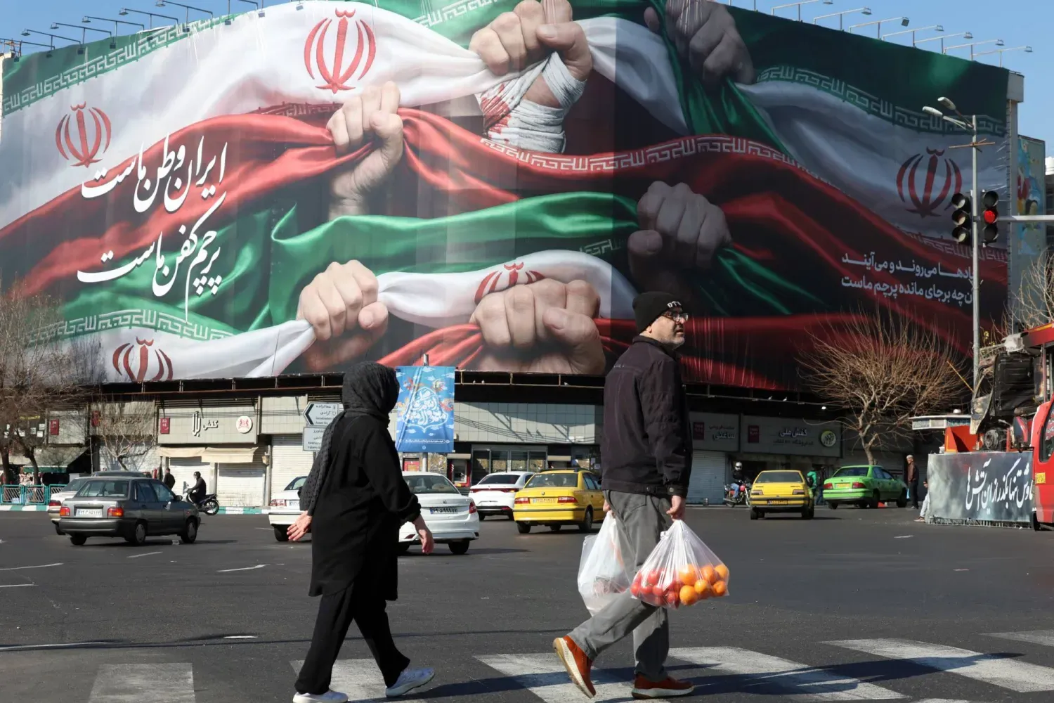  ‘İran bizim vatanımızdır’ yazan Farsça bir reklam panosunun önünden geçen İranlılar (EPA)