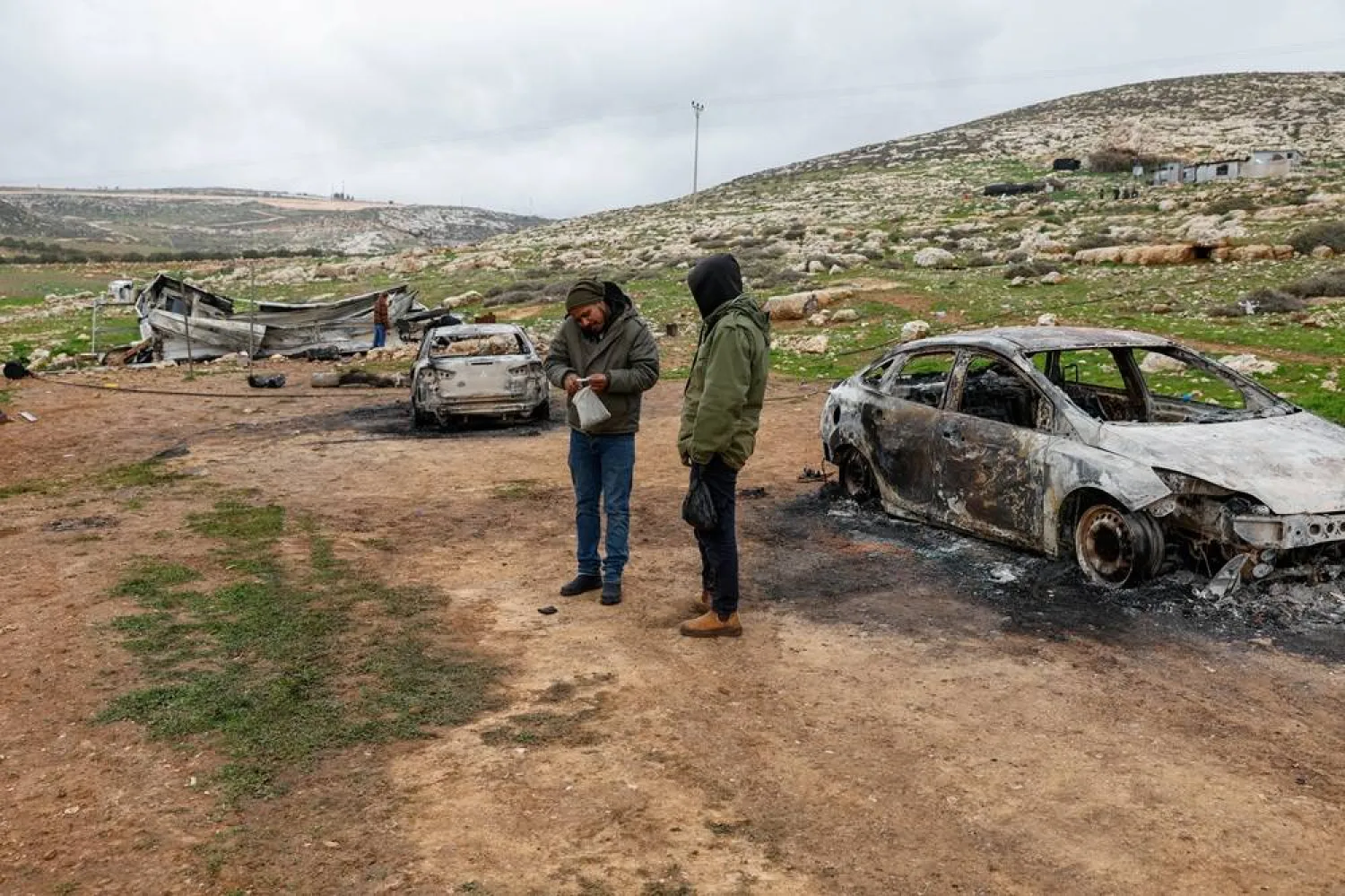  People stand in an area with destroyed vehicles and a structure, which Palestinians say were burned by Israeli settlers on Saturday, in the Palestinian town of Mikhmas, near Ramallah in the Israeli-occupied West Bank, January 18, 2026. (Reuters)