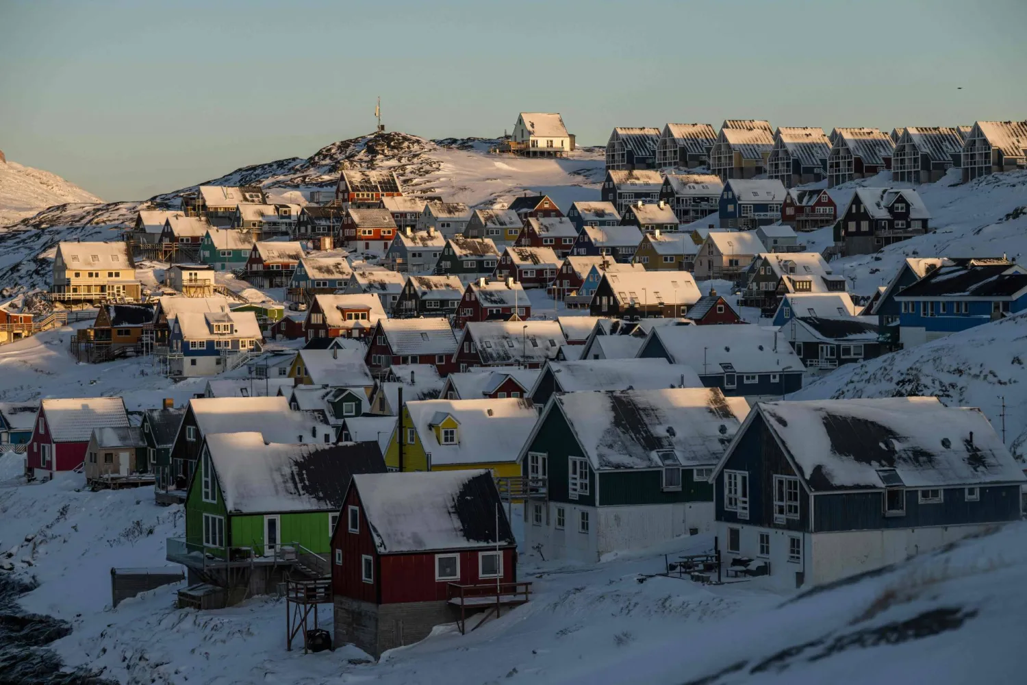 Snow-covered houses line a hillside in Nuuk, Greenland, as warm evening light hits the neighborhood on January 20, 2026. (AFP)