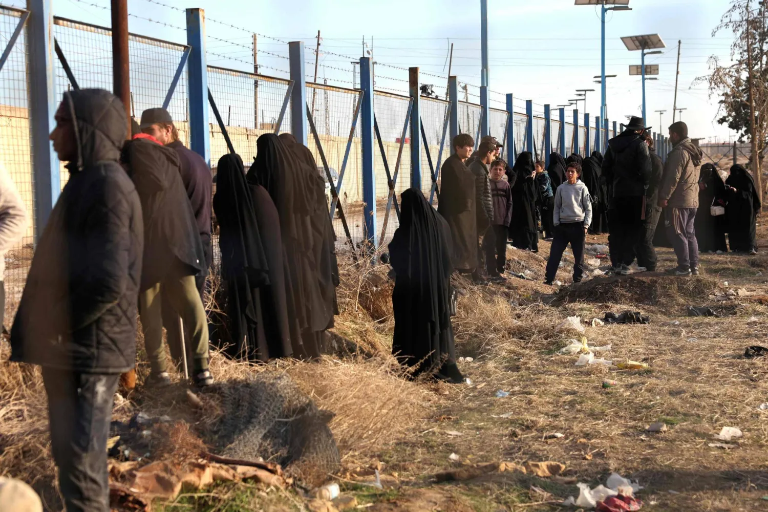 Relatives of suspected ISIS detainees, stand behind a fence in al-Hol camp in the desert region of Syria's Hasakeh province on January 21, 2026. (AFP)