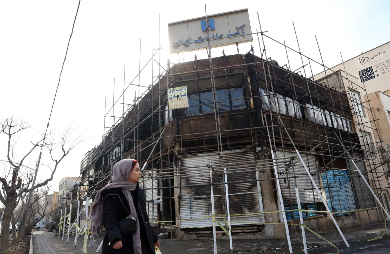 إيرانية تمر أمام فرع لبنك صادرات تضرر جراء حريق اندلع خلال الاحتجاجات (إ.ب.أ)