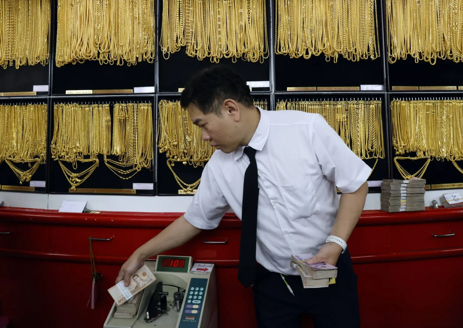 صائغ ذهب يعدّ الأوراق النقدية خلال عملية تداول الذهب في متجر للذهب في بانكوك  (إ.ب.أ)