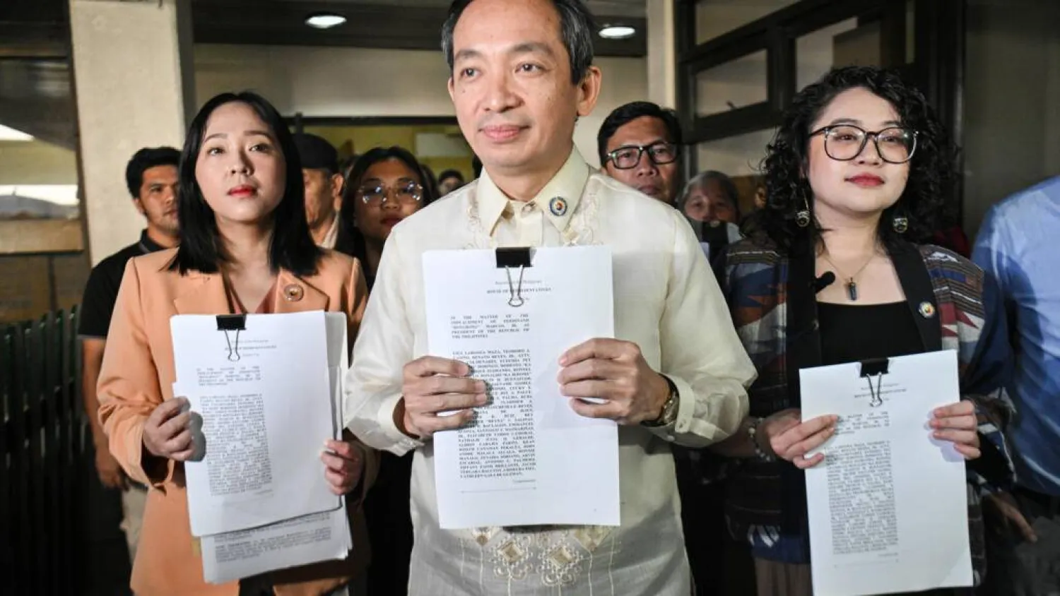Lawmakers Sara Elago, Antonio Tinio and Louise Co show the impeachment complaint against Philippine President Ferdinand Marcos at the House of Representatives on Thursday. TED ALJIBE / AFP
