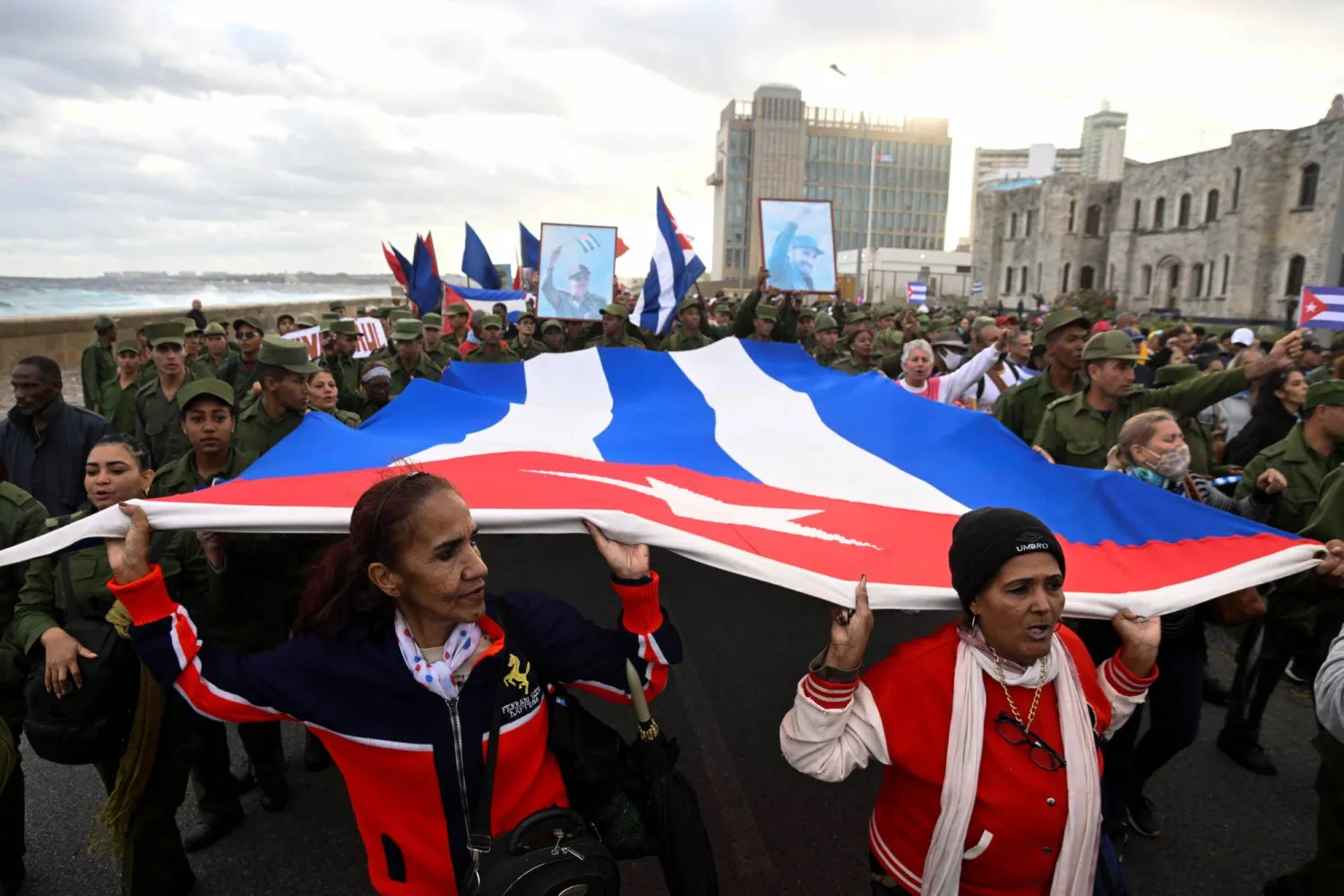 عسكريون ومدنيون يحملون علماً كوبياً كبيراً خلال مسيرة أمام السفارة الأميركية احتجاجاً على ما وصفوه بـ«العدوان الأميركي» في المنطقة (رويترز)