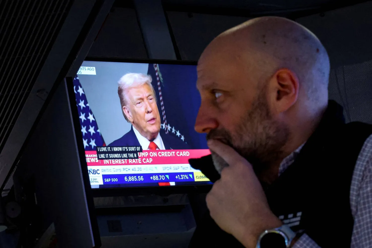 شاشة تعرض دونالد ترمب وهو يجري مقابلة خلال اجتماع المنتدى الاقتصادي العالمي في دافوس بينما يعمل أحد المتداولين بقاعة بورصة نيويورك (رويترز)