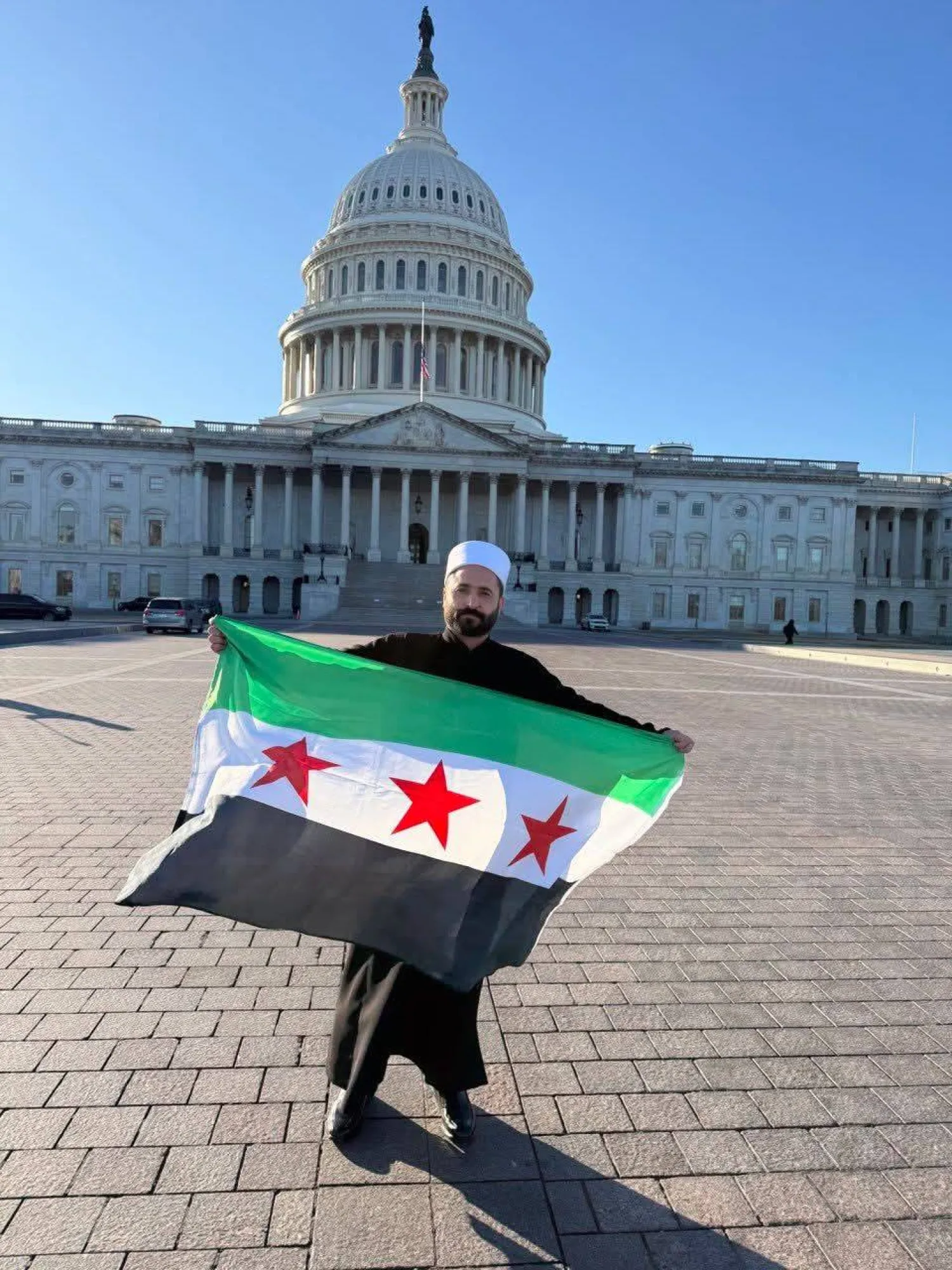 سليمان عبد الباقي مدير الأمن الداخلي في السويداء يرفع العلم السوري أمام مبنى الكونغرس في واشنطن (إكس)