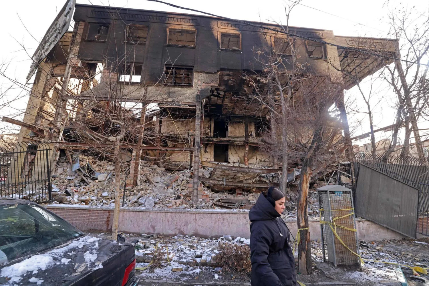 This photograph taken during a tour for foreign media shows a woman walking past a government building that was burned during recent public protests, in Tehran on January 21, 2026. (AFP)