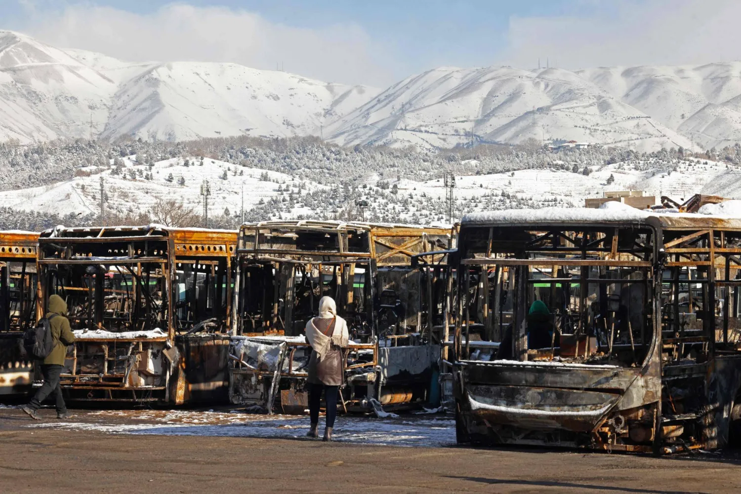 This photograph taken during a tour for foreign media shows media representatives walking past the parked buses that were burned at a depot during recent public protests, in Tehran on January 21, 2026. (AFP)