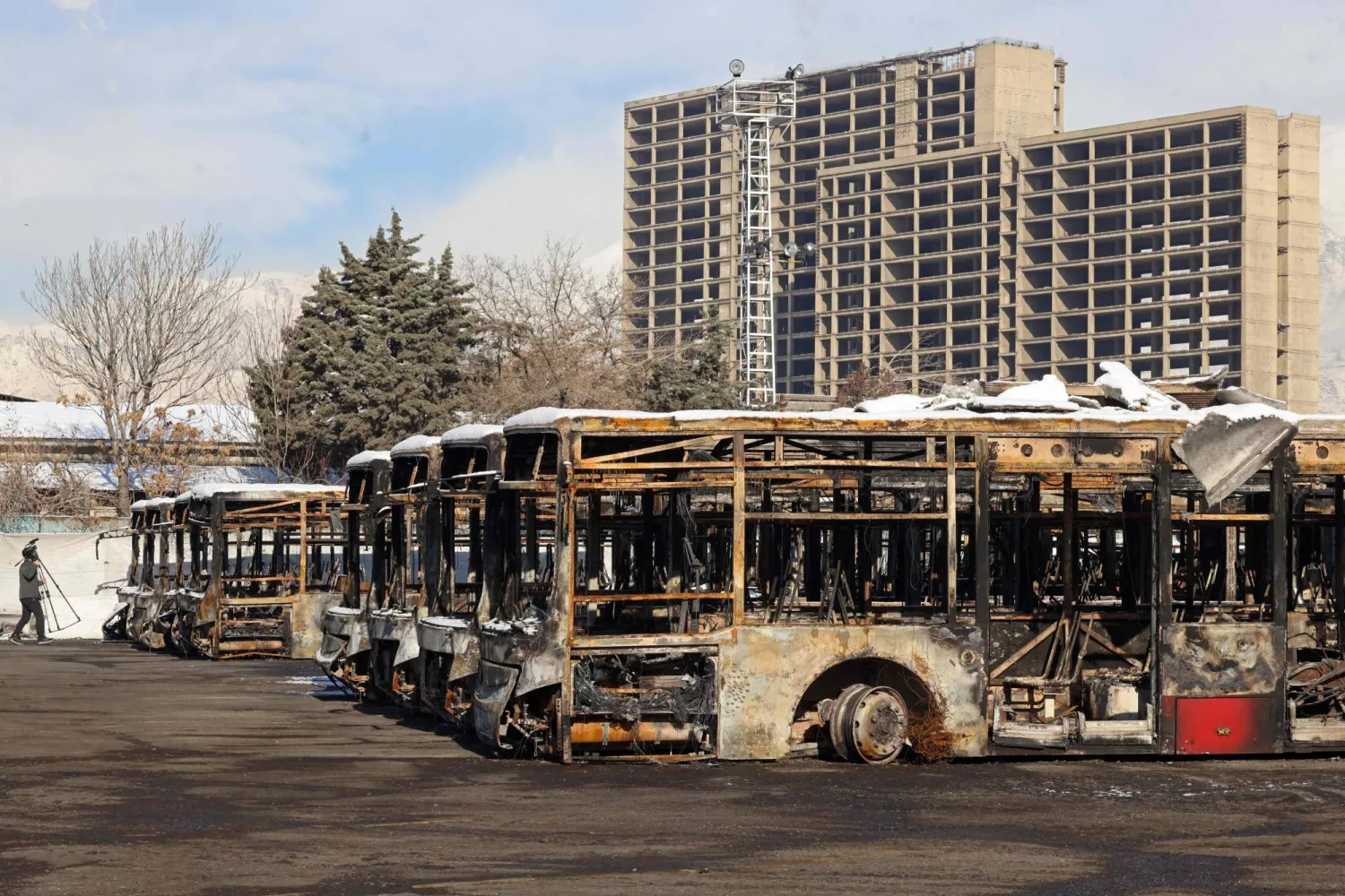 This photograph taken during a tour for foreign media shows a media representative walking past the parked buses that were burned at a depot during recent public protests, in Tehran on January 21, 2026. (AFP)