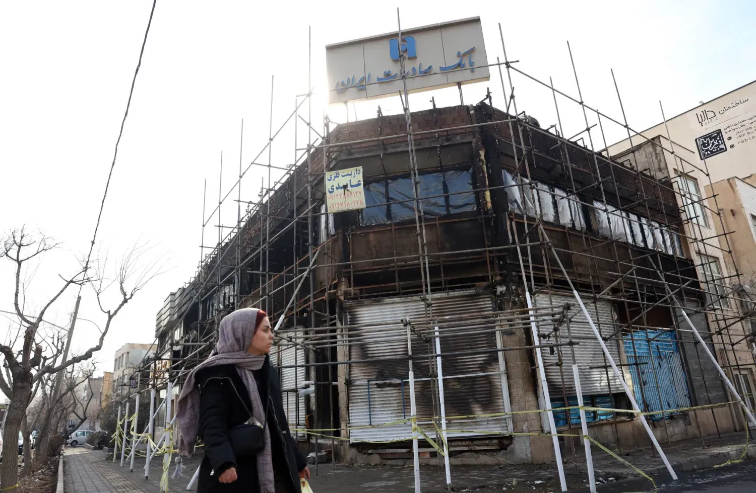 İranlı bir kadın, Tahran'da son dönemdeki hükümet karşıtı protestolar sırasında çıkan yangında hasar gören bir banka binasının önünden geçiyor (EPA)