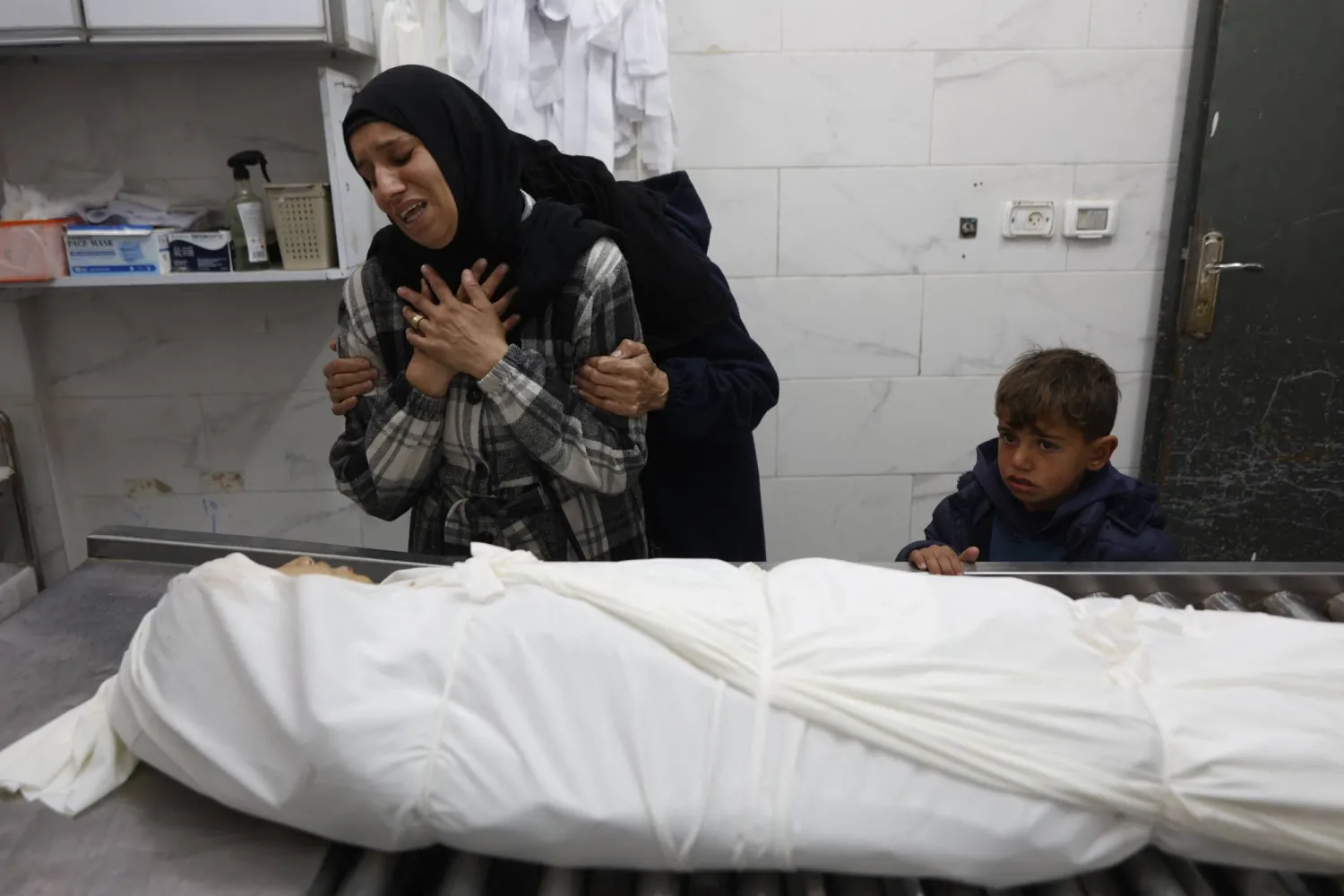 Palestinian Hadeel al-Zawarah (front), 33, mother of Salman, 13-years-old is comforted by Asma Al-Zawra, 37, mother of 15-year-old, Mohammed, as they both grieve over the bodies of their sons killed in an Israeli drone strike, at the morgue of the Al-Shifa Hospital in Gaza City, on January 24, 2026. (AFP)