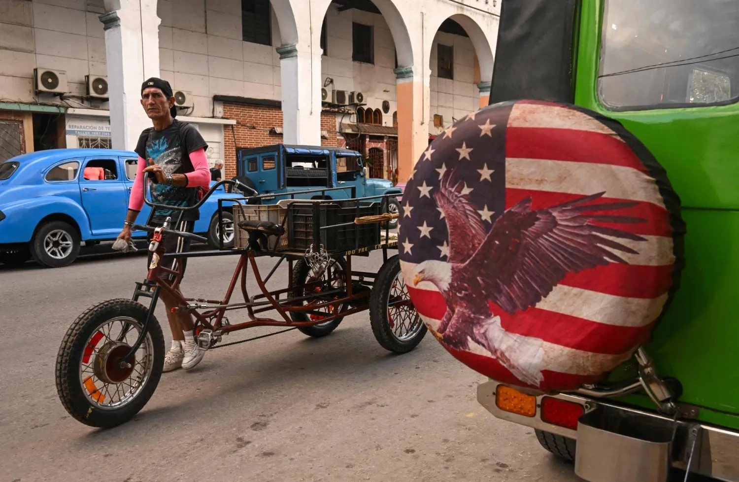  A man pushes a tricycle past a jeep sporting a wheel cover with an image based on the US flag in Havana on January 23, 2026. (AFP)