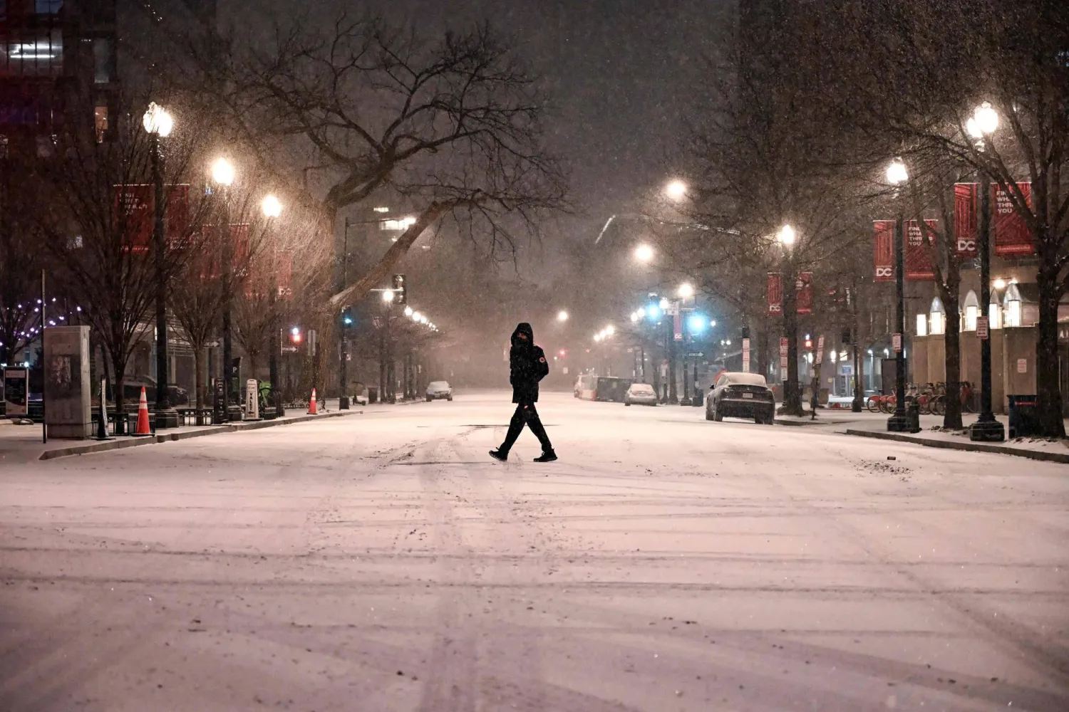Snow falls as a person crosses a street in downtown Washington, DC, on January 25, 2026. (AFP)