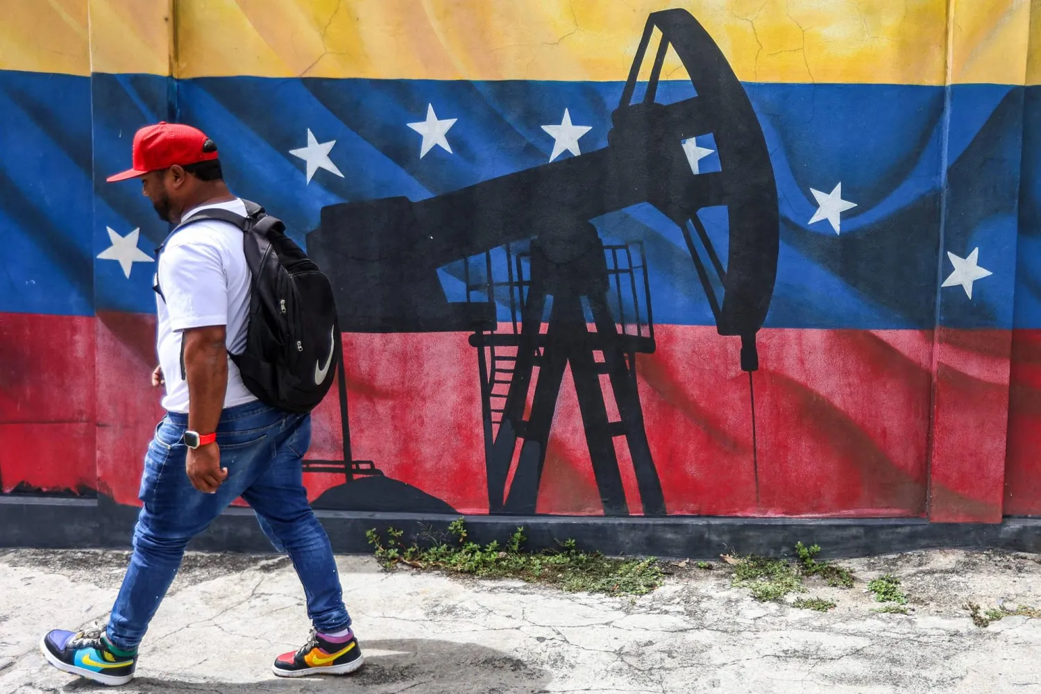 A man walks past a mural depicting an oil pumpjack on a Venezuelan flag in Caracas on January 15, 2026. (AFP)