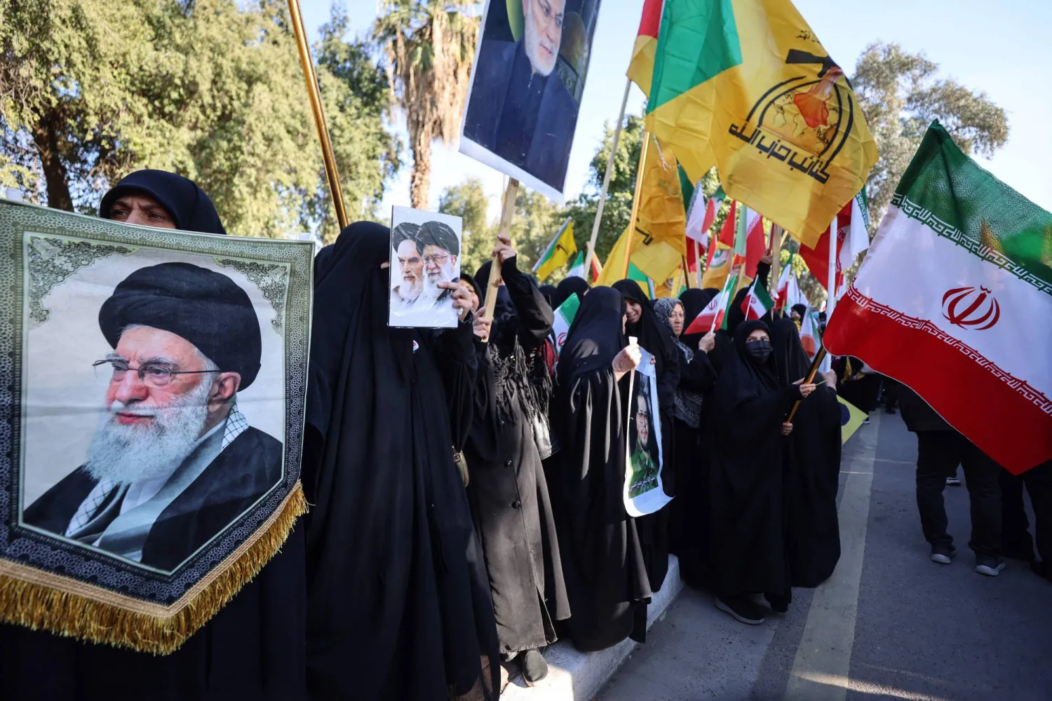 عراقيون يحملون علم إيران وشعار «كتائب حزب الله» وصورة خامنئي خلال مظاهرة في بغداد (أ.ف.ب)