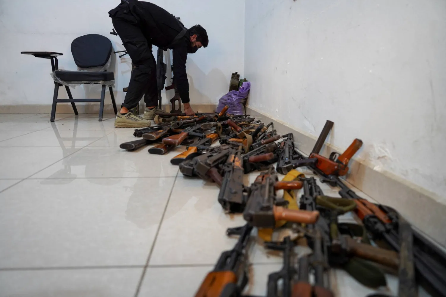 أحد أفراد قوات الأمن السورية يضع سلاحاً على الأرض بجوار أسلحة تم جمعها في الرقة بسوريا في 27 يناير 2025 (رويترز)