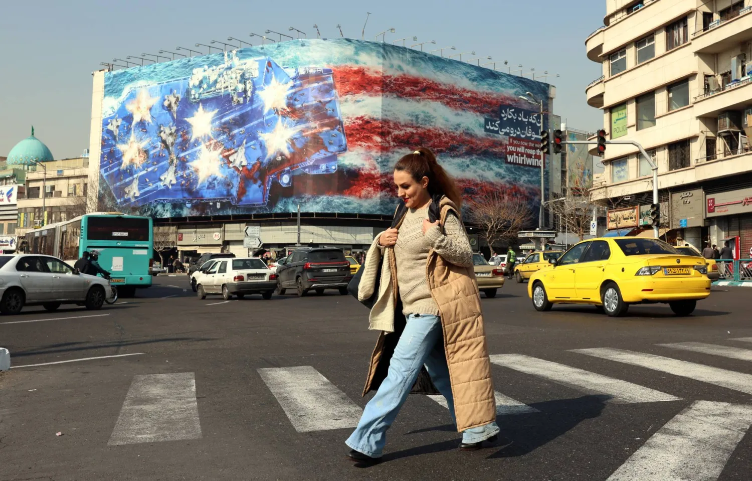 إيرانية تعبر ساحة «انقلاب» وسط طهران بالقرب من لافتة ضخمة مناهضة للولايات المتحدة (إ.ب.أ)