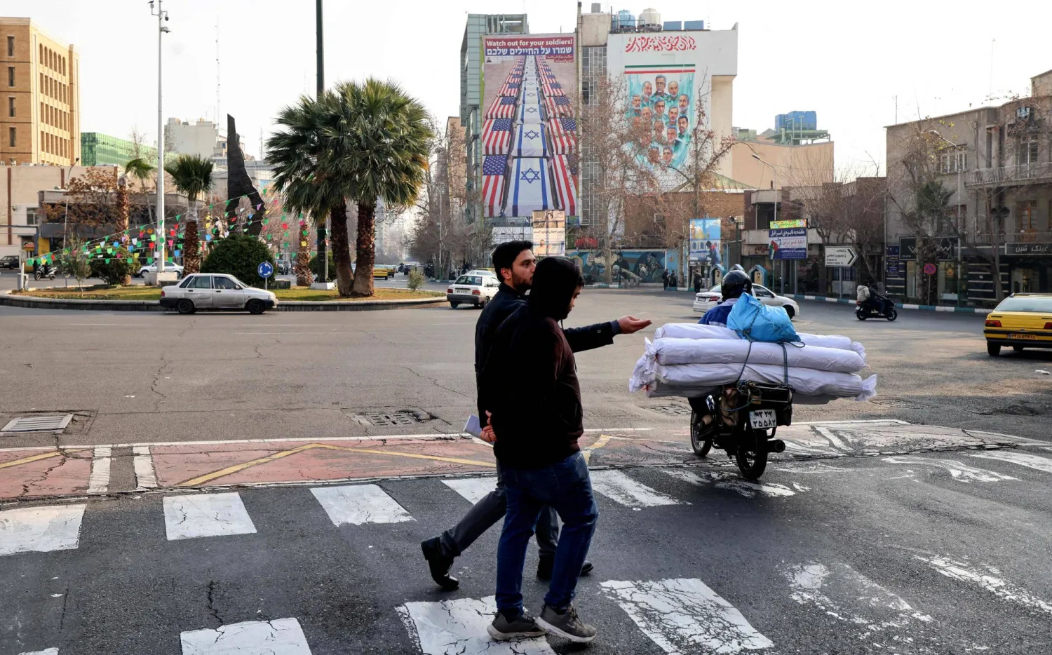 Iranian men walk past an anti-US and anti-Israel banner hanging on a building in Palestine Square in Tehran on January 27, 2026. (AFP)