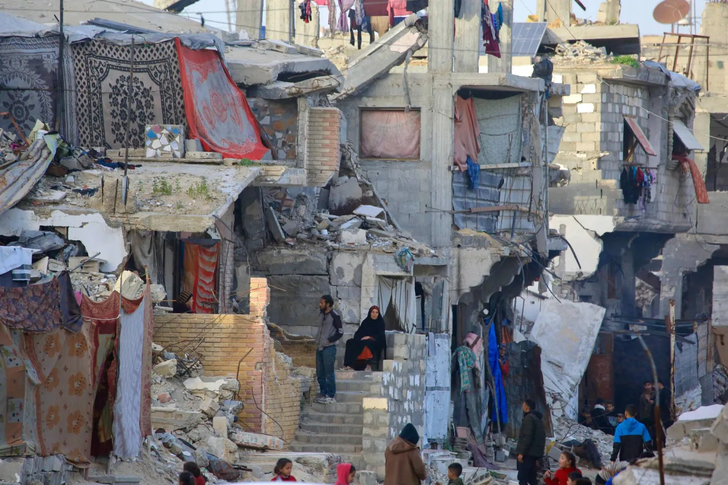 فلسطينيون يجلسون وسط المنازل المدمرة في خان يونس (أ.ف.ب)