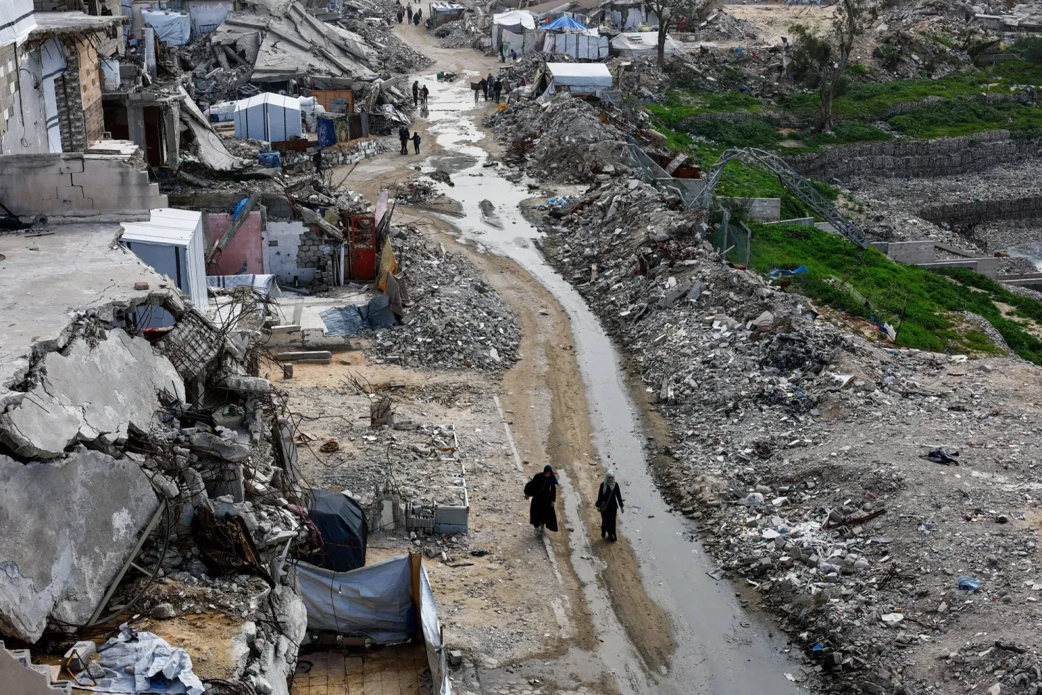 Filistinliler, Çarşamba günü Gazze’de İsrail’in yıktığı konut binalarının enkazları arasında yürüyor (Reuters)