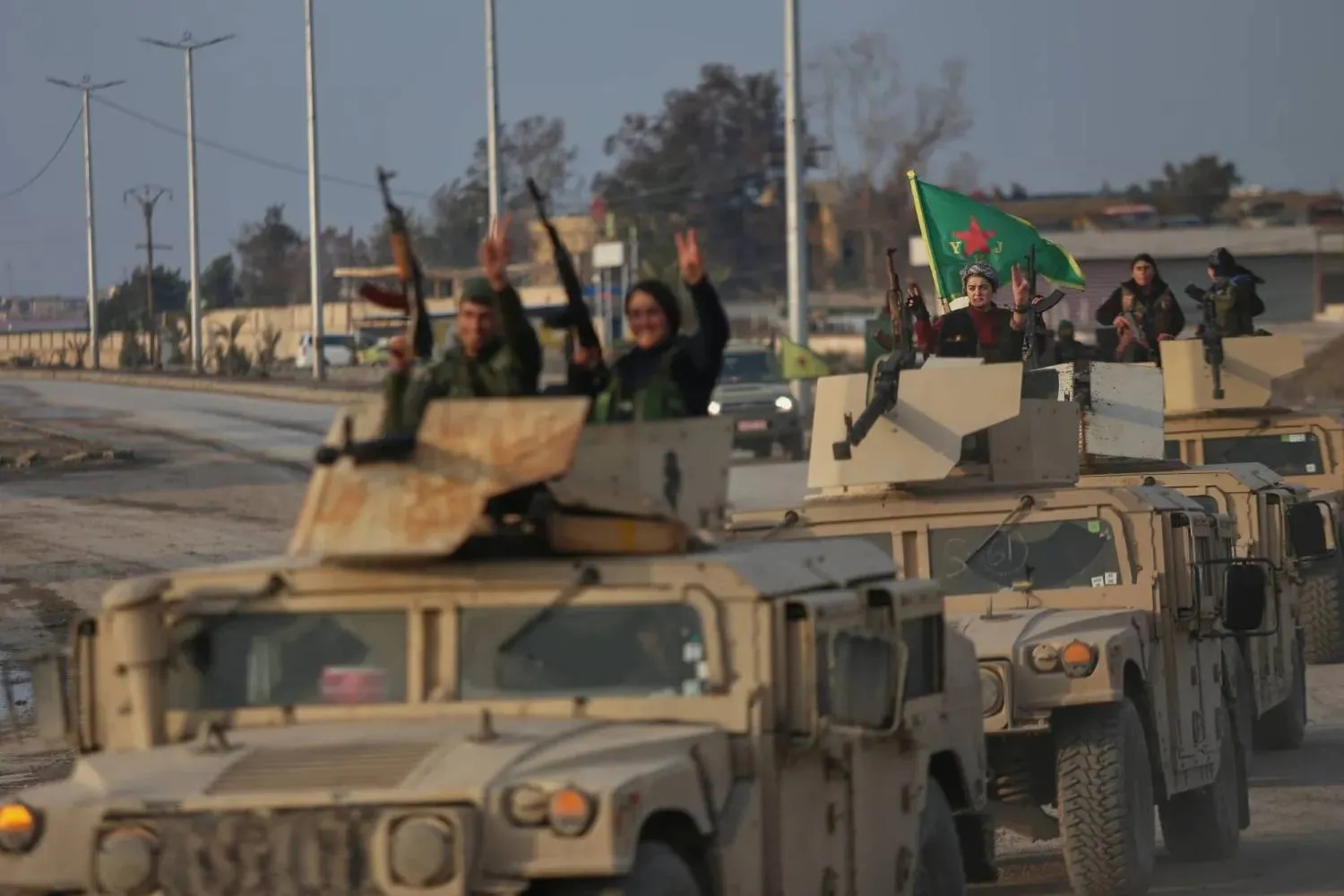Kurdish fighters aboard Syrian Democratic Forces military vehicles flash victory signs in Hasakah (AP)   