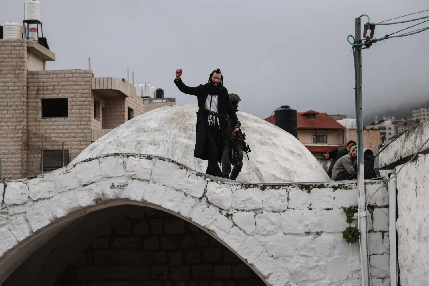 يهودي يلوّح فوق قبر يوسف بمدينة نابلس في شمال الضفة الغربية المحتلة (أ.ف.ب)