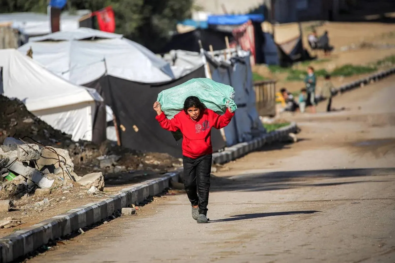 A young girl carries a bag on her back as she walks along a road in the Nuseirat Palestinian refugee camp north of Deir al-Balah in central Gaza. (AFP)