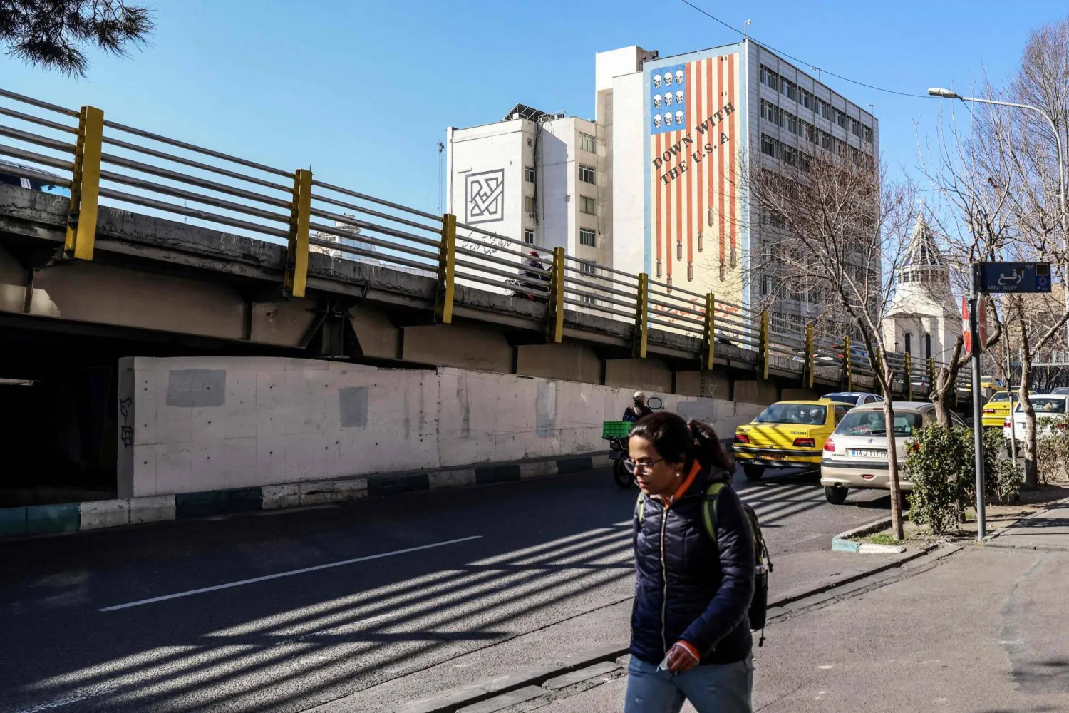 An Iranian walks past a huge anti-US mural painted on the side of a building in the Iranian capital Tehran on January 31, 2026. (Photo by Atta KENARE / AFP)