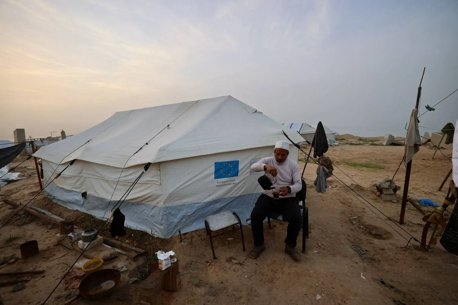 رجل يسكب مشروباً ساخناً خارج خيمة في مخيم النصيرات للاجئين الفلسطينيين وسط قطاع غزة (أ.ف.ب)