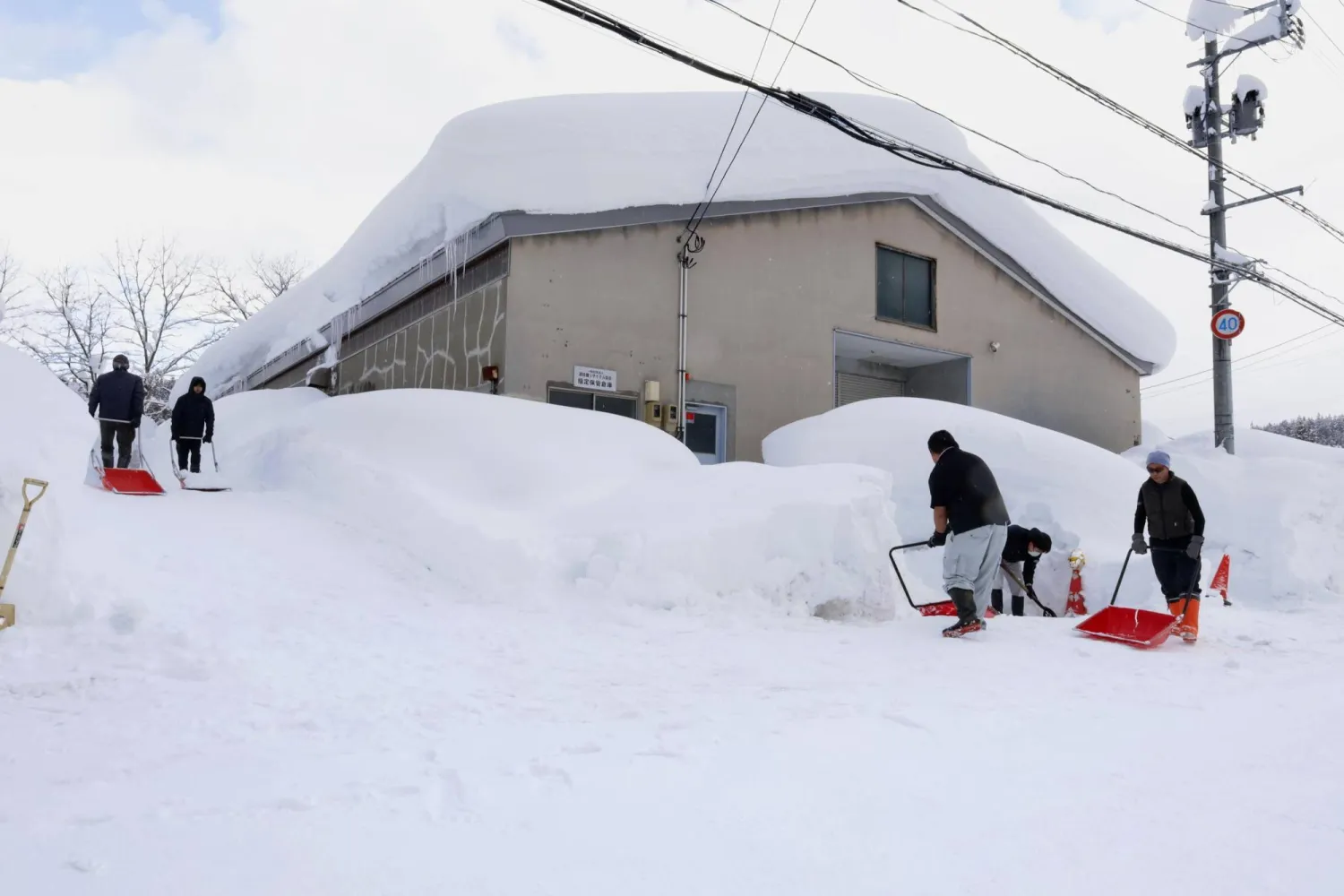  People clear snow near a building in Aomori, northern Japan, Monday, Feb. 2, 2026. (Kyodo News via AP)