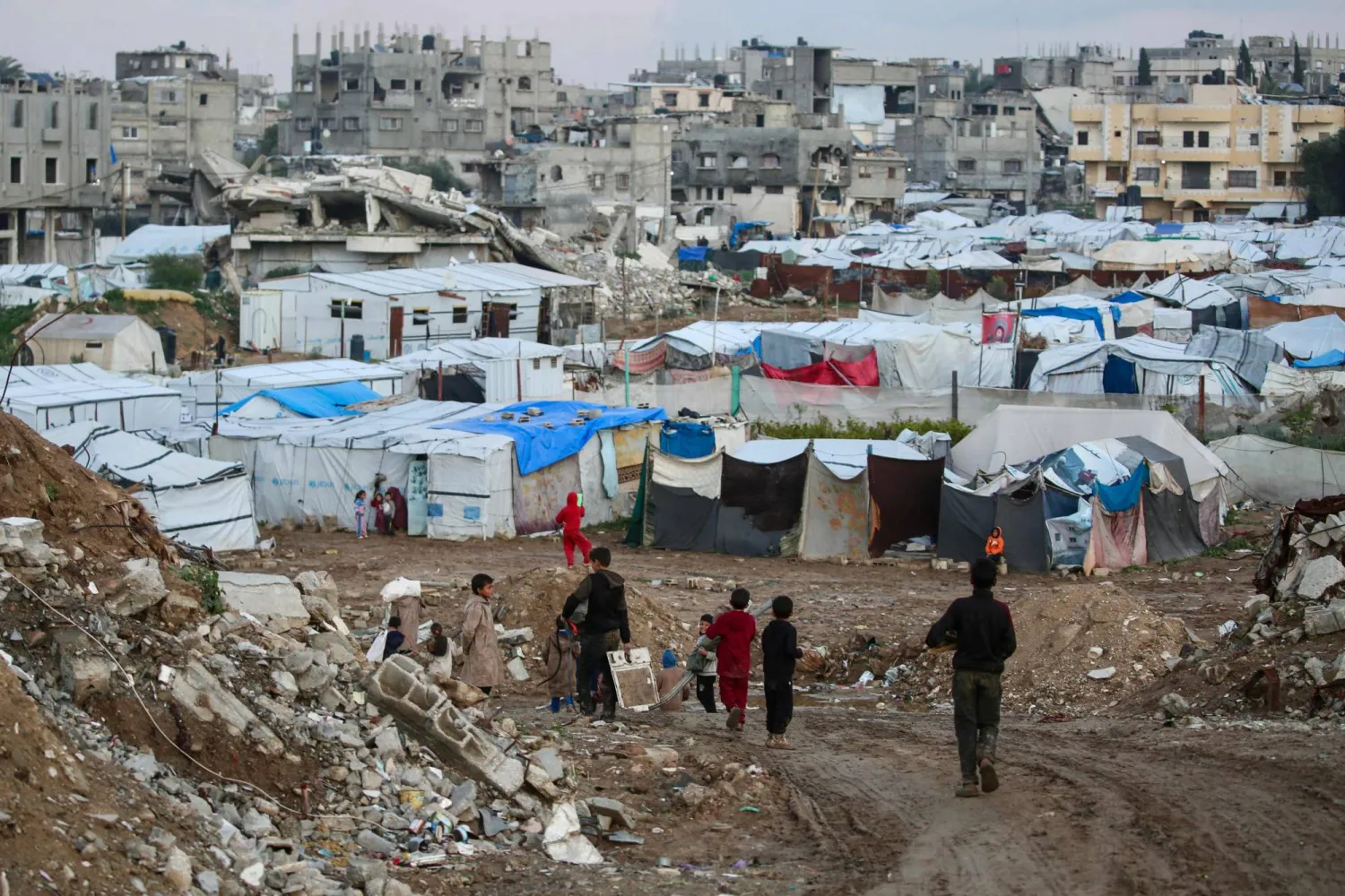Children walk past tents and makeshift shelters in the Bureij refugee camp in the central Gaza Strip on February 3, 2026. (Photo by Eyad BABA / AFP)