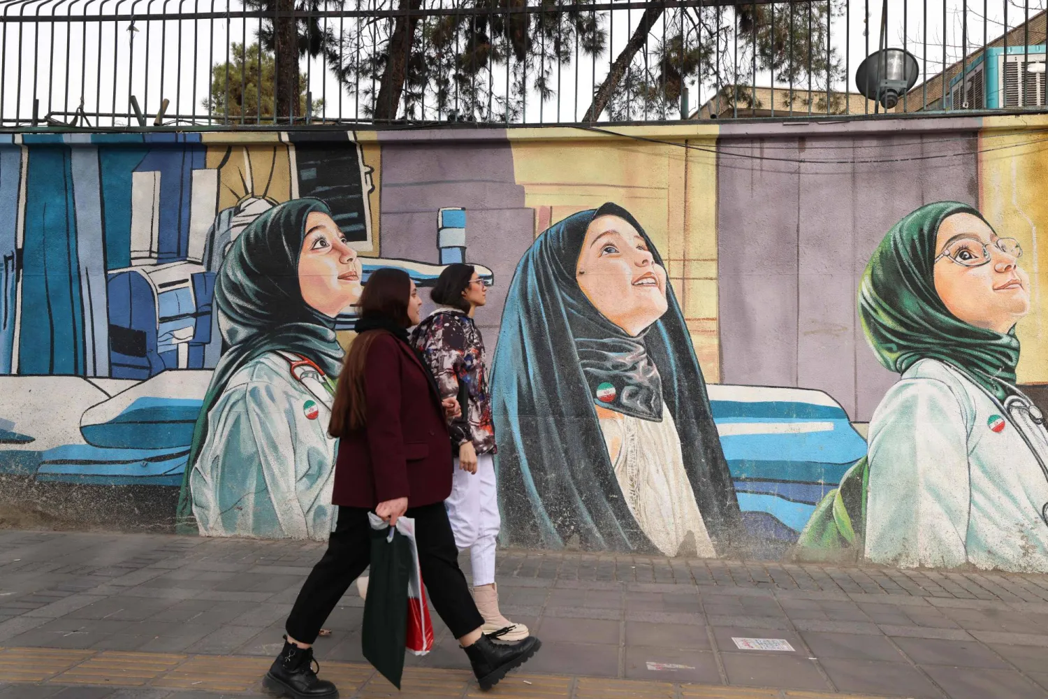 Women walk past a mural depicting children as future scientists in Tehran on February 3, 2026. (Photo by ATTA KENARE / AFP)