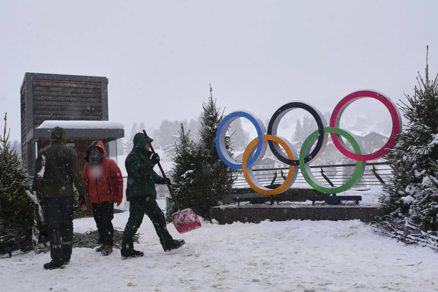 أشخاص يعملون بالقرب من الحلقات الأولمبية المعروضة استعداداً لدورة الألعاب الأولمبية الشتوية 2026 (أ.ب)