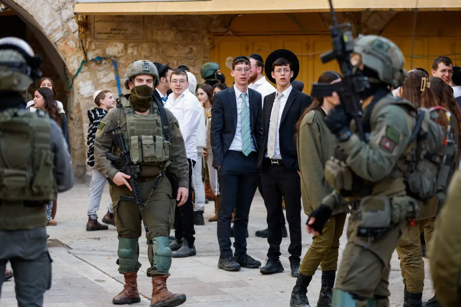 İsrailli yerleşimciler, işgal altındaki Batı Şeria'da bulunan Hebron'da 31 Ocak 2026'da haftalık devriye sırasında nöbetteki İsrail askerlerini izliyor (Reuters)