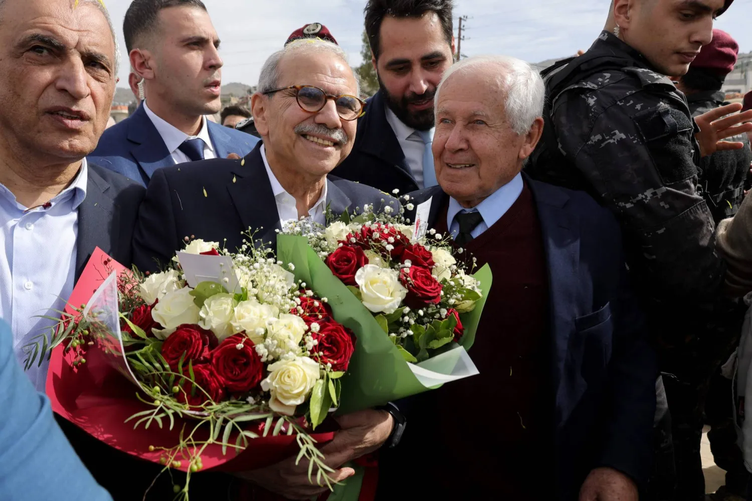 Lebanon's Prime Minister Nawaf Salam (L) holds bouquets of flower as he stands next to the mayor of the heavily-damaged southern village of Kfar Shouba, near the border with Israel, during his visit on February 8, 2026. (AFP)