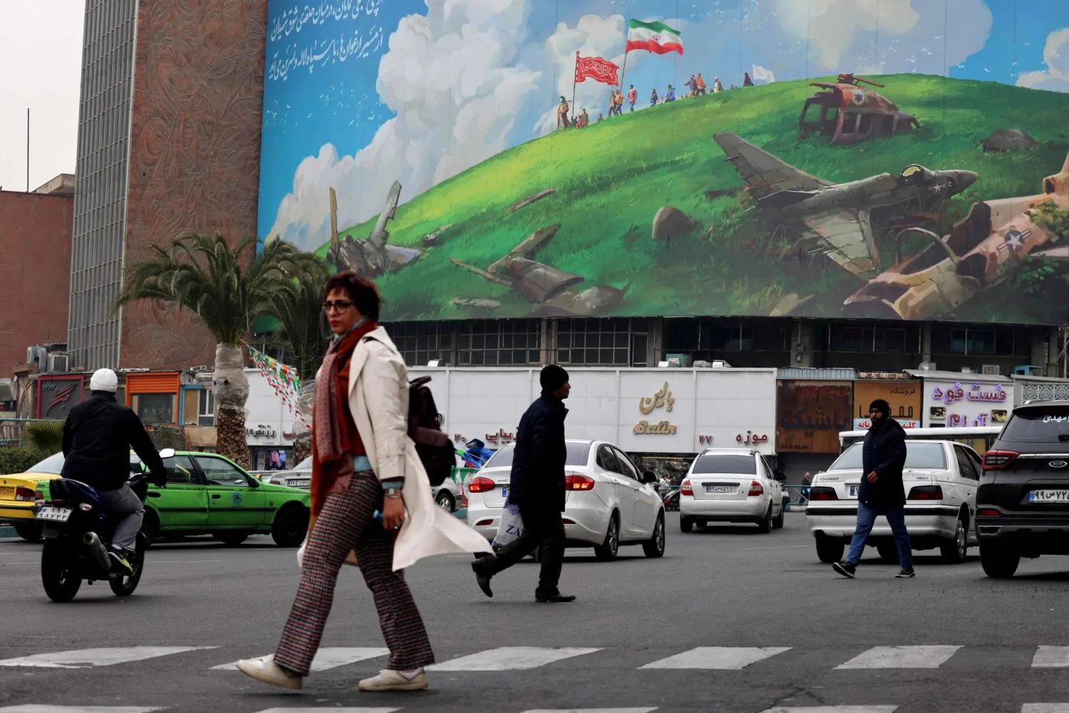 People walk past a huge anti-US billboard displayed on a building in Tehran's Valiasr Square on February 8, 2026. (Photo by ATTA KENARE / AFP)