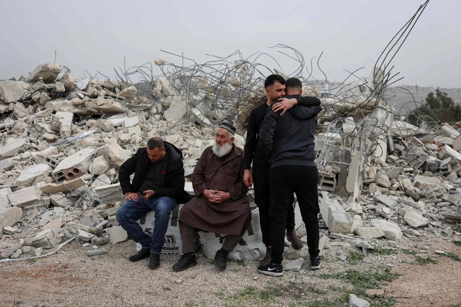 Palestinian men sit on the rubble as others console each other after a Palestinian home was demolished by the Israeli army in the village of Shuqba, west of the city of Ramallah, in the Israeli-occupied West Bank on February 9, 2026. (Photo by Zain JAAFAR / AFP)