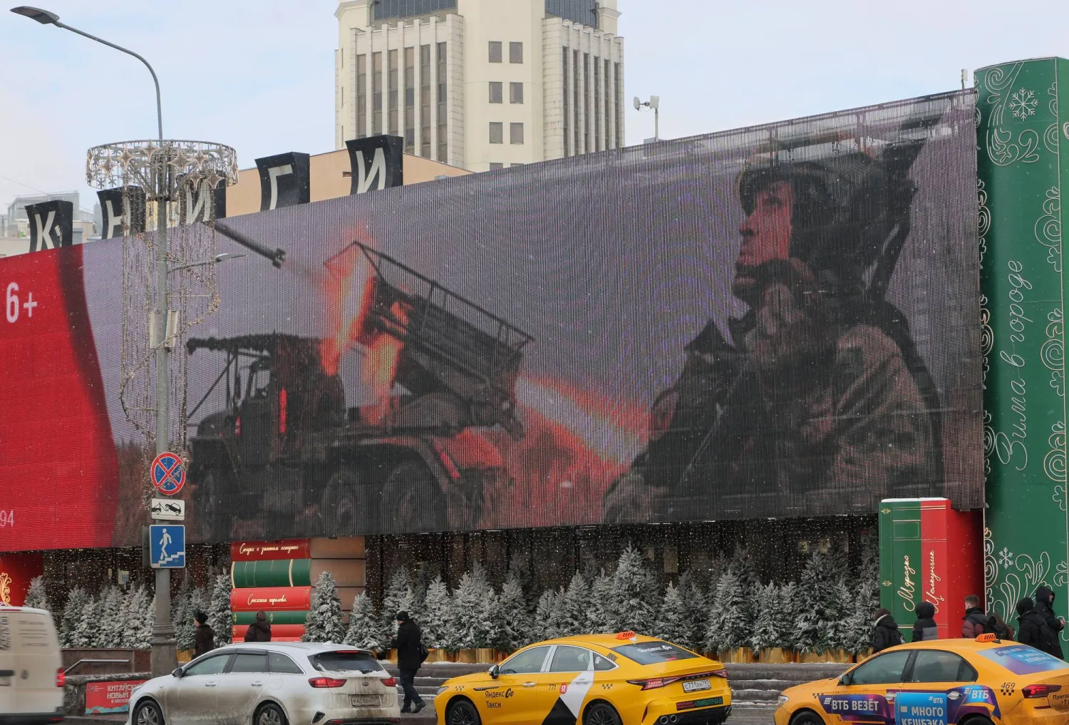 أشخاص يسيرون في أحد شوارع المدينة في موسكو بينما تعرض شاشة إلكترونية صورة جندي روسي (إ.ب.أ)