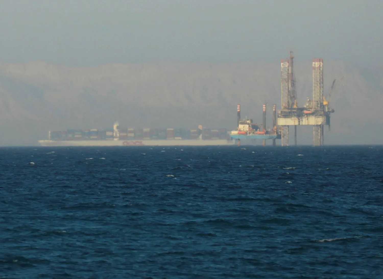 سفينة حاويات تمر بجوار منصة نفطية في خليج السويس (رويترز)