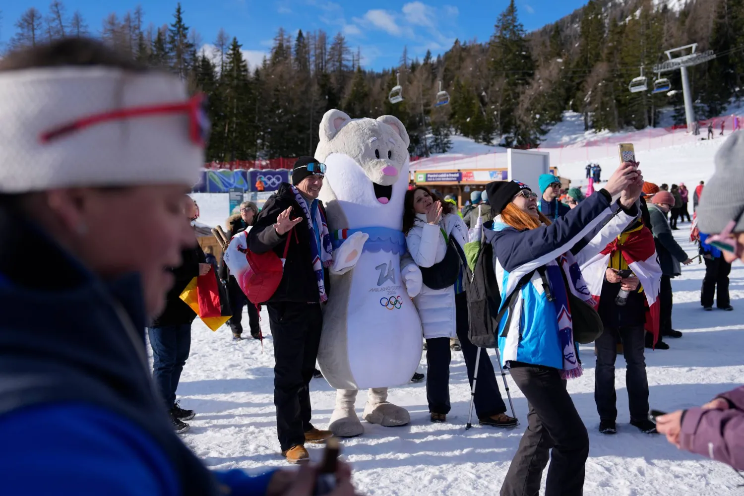 Fans take selfies with the Olympic mascot Tina at the finish area of an alpine ski, slalom portion of a women's team combined race, at the 2026 Winter Olympics, in Cortina d'Ampezzo, Italy, Tuesday, Feb. 10, 2026. (AP)
