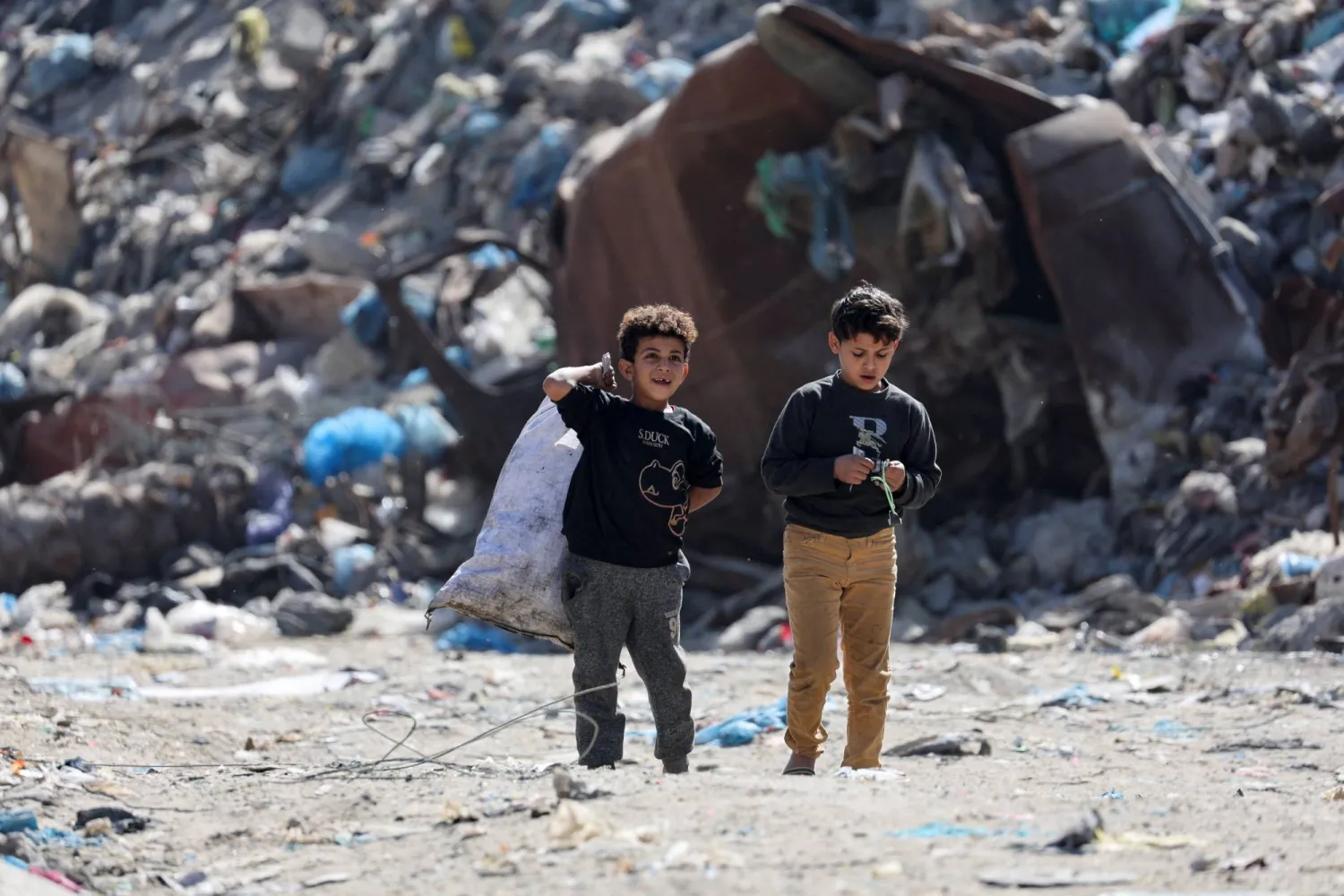 طفلان فلسطينيان يسيران قرب مكب نفايات في مدينة غزة يوم الأربعاء (رويترز)