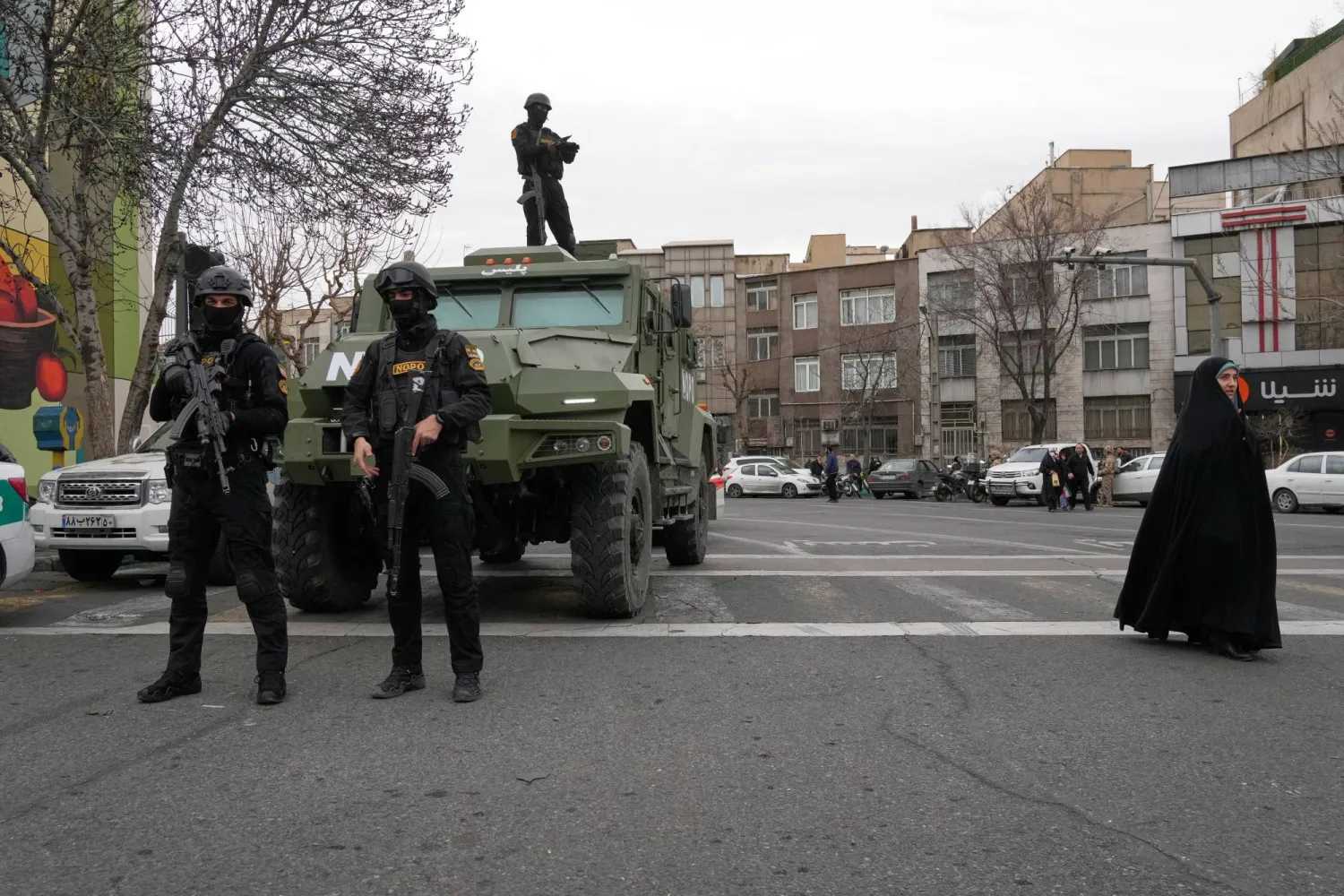 Policemen stand guard during an annual rally marking 1979 Iranian Revolution as a woman walks at right at the Azadi (Freedom) St. Tehran, Iran, Wednesday, Feb. 11, 2026. (AP Photo/Vahid Salemi)