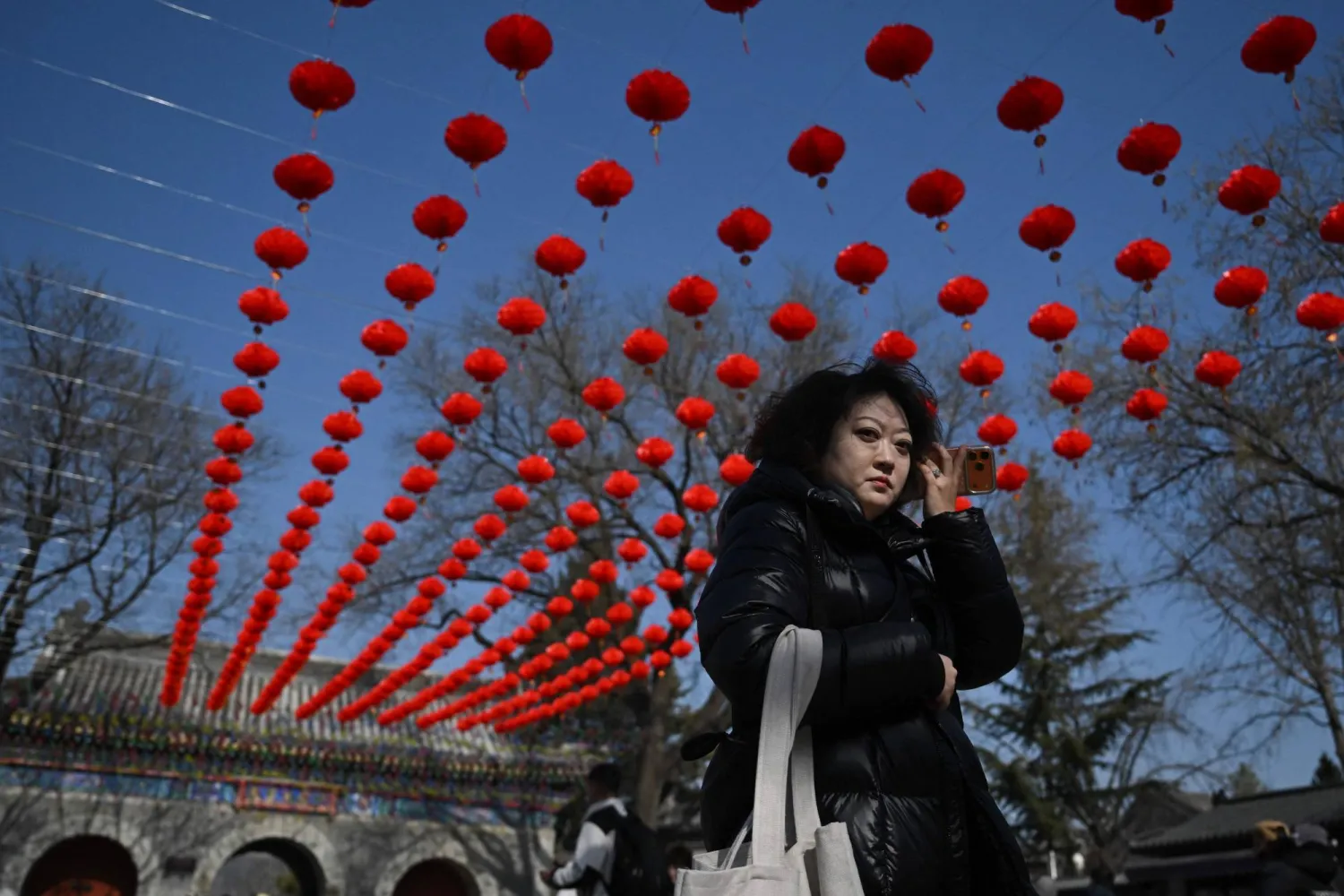 امرأة تسير تحت زينة العام الجديد بأحد المعابد في العاصمة الصينية بكين (أ.ف.ب)
