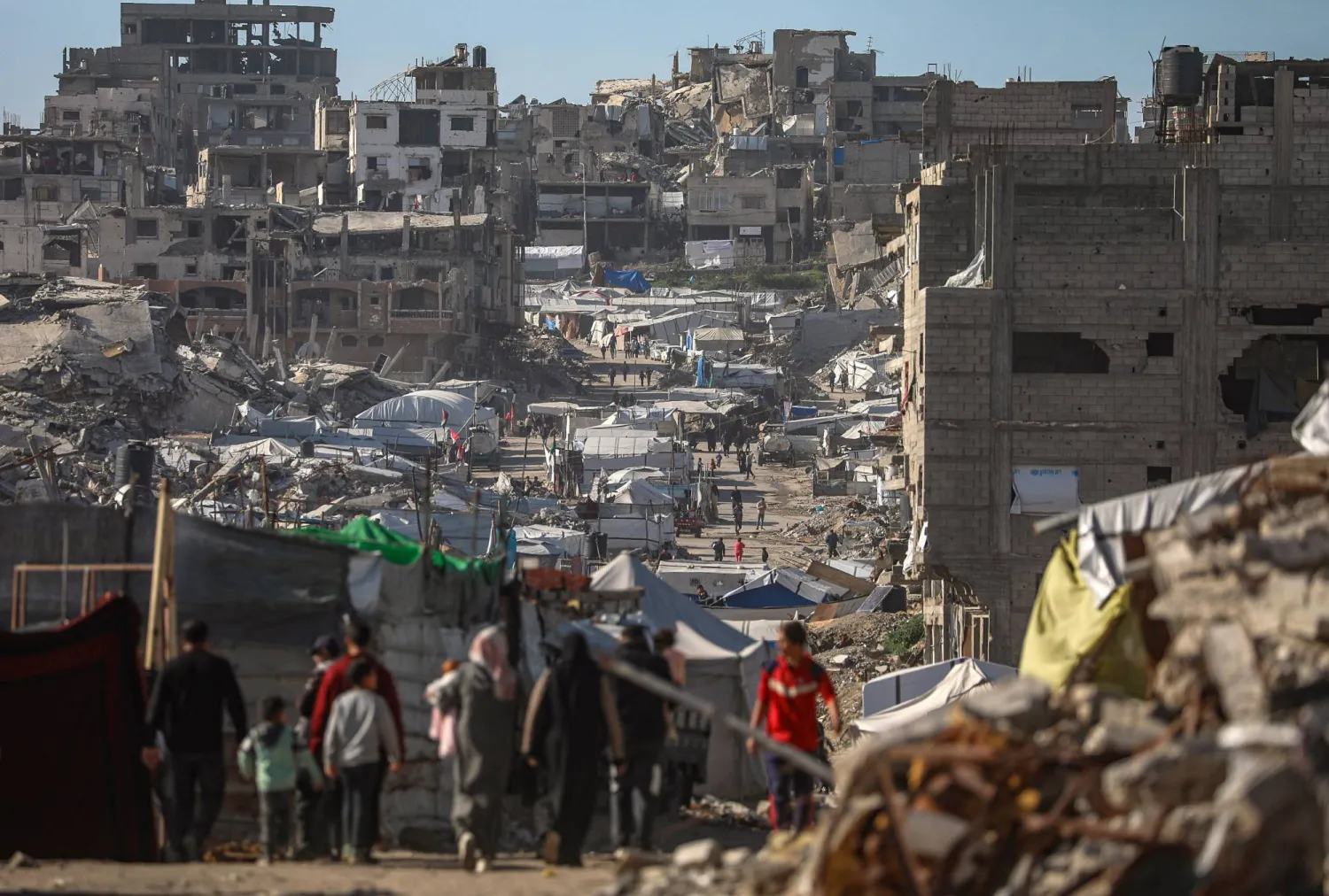 فلسطينيون نازحون داخلياً يسيرون بين أنقاض حي التفاح شرق مدينة غزة (إ.ب.أ)