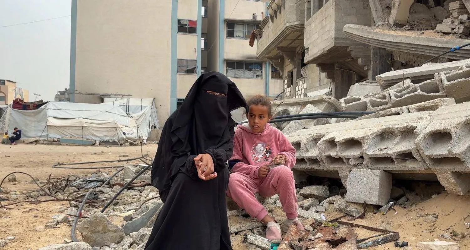 ضحى أبو سنيمة ووالدتها تجلسان بجوار منزل مهدم (الشرق الأوسط)