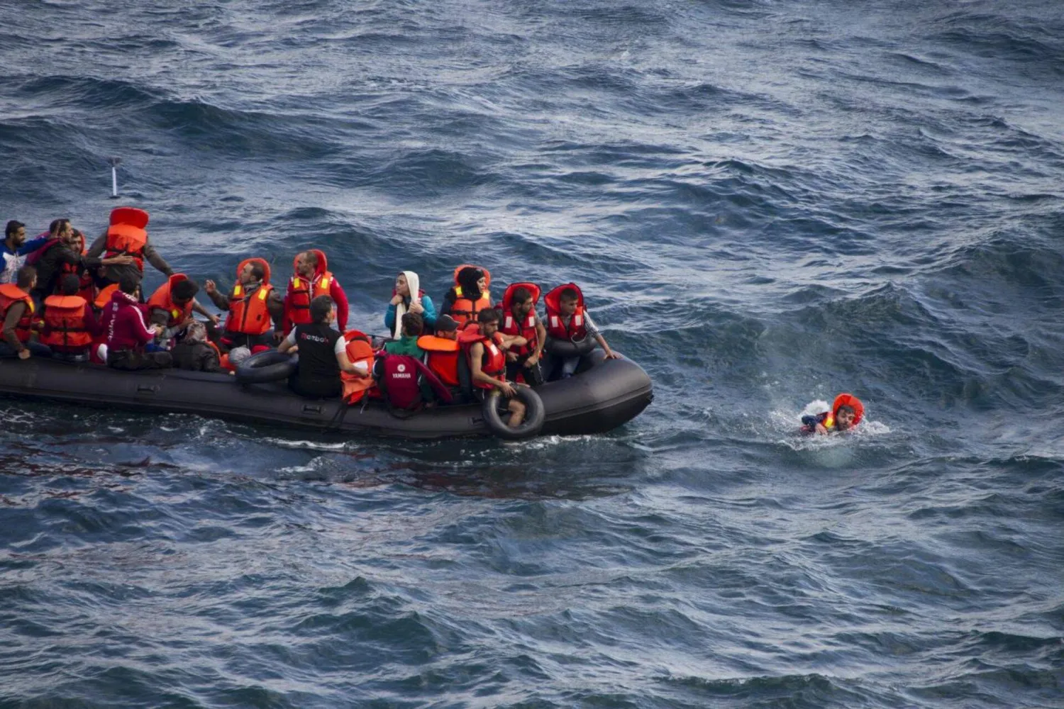 مهاجر يسبح بجوار قارب مطاطي مكتظ بالمهاجرين قرب شواطئ جزيرة ليسبوس اليونانية أثناء عبوره جزءاً من بحر إيجه من الساحل التركي (رويترز - أرشيفية)